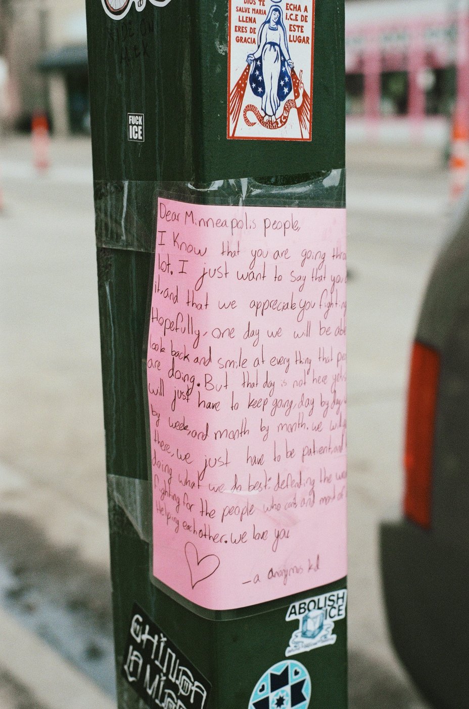 A handwritten note taped to a street pole at the memorial for Alex Pretti, Minneapolis, March 10, 2026
